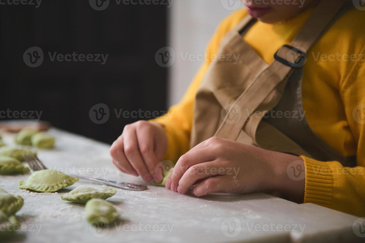 de cerca manos de un pequeño niño niña en el rural cocina, esculpe empanadillas desde masa con machacado patatas relleno. Cocinando hecho en casa vegetariano albóndigas, italiano Ravioles o ucranio varenyky foto