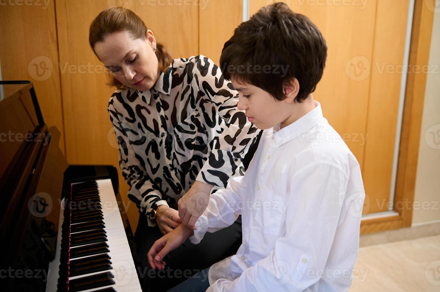 Handsome teenage boy taking piano lesson, passionately playing the keys under her teacher's guidance, feeling the rhythm of music. Musical education and talent development in progress photo