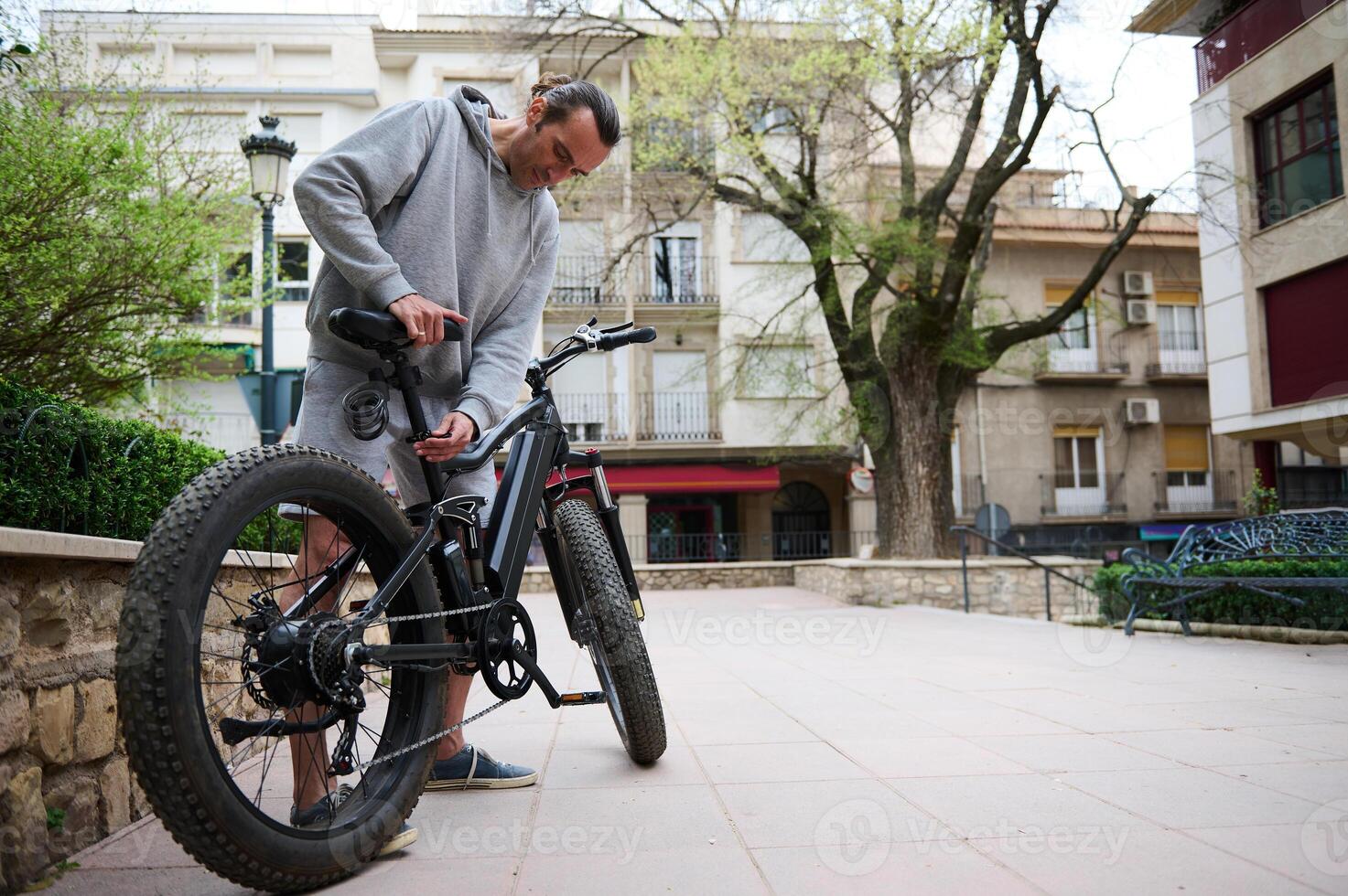 Caucasian young man adjusts the height of new battery powered bike, electric bicycle before taking it out for first ride photo