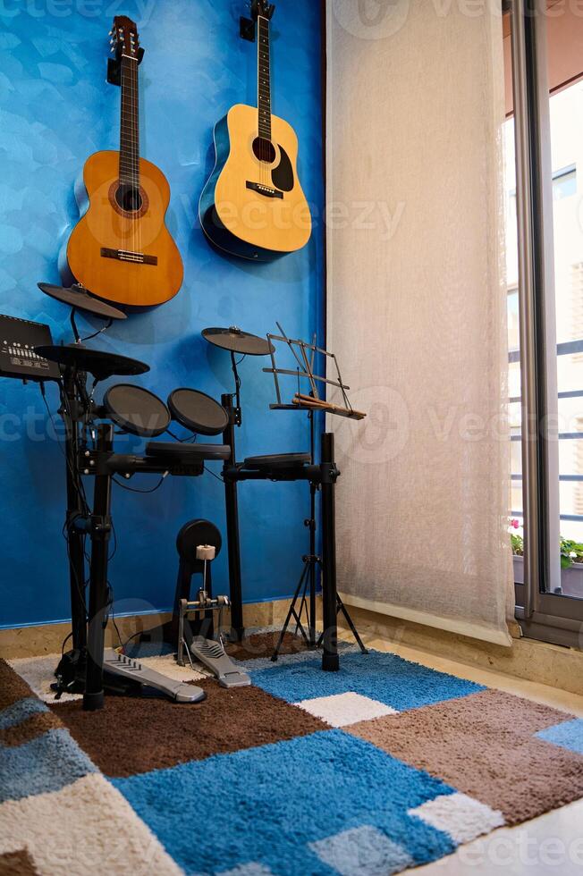 Modern interior of a music studio for home use. Acoustic nd electric guitars hanging on blue color wall and drum set. Hobbies and leisure. Musician's room for playing and learning music photo