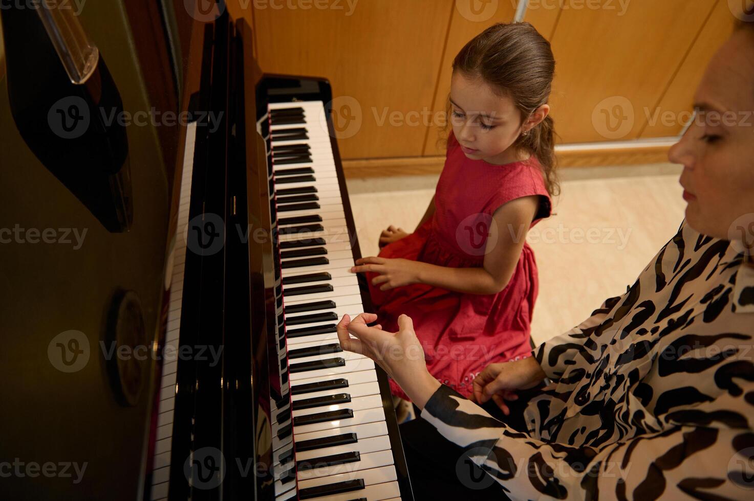 Little child girl having a piano lesson with her teacher. Female pianist explaining the correct position of hands on piano keys. photo