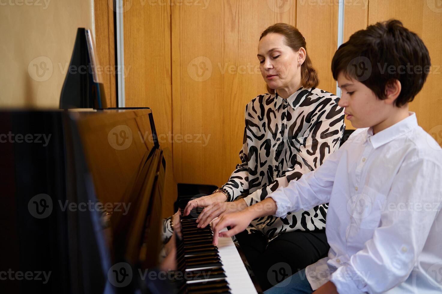 Authentic portrait of a young adult mother and son sitting at grand piano, performing classic melody, toucher white and black keyboard of the piano forte, playing piano, singing song photo