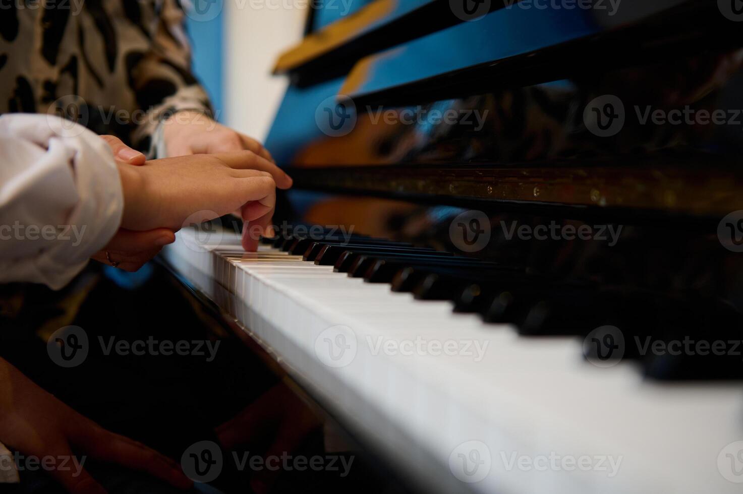 Side view hands of musician pianist teacher maestro teaching a child boy the true position of fingers on piano keys while performing musical composition on grand pianoforte, during music lesson photo