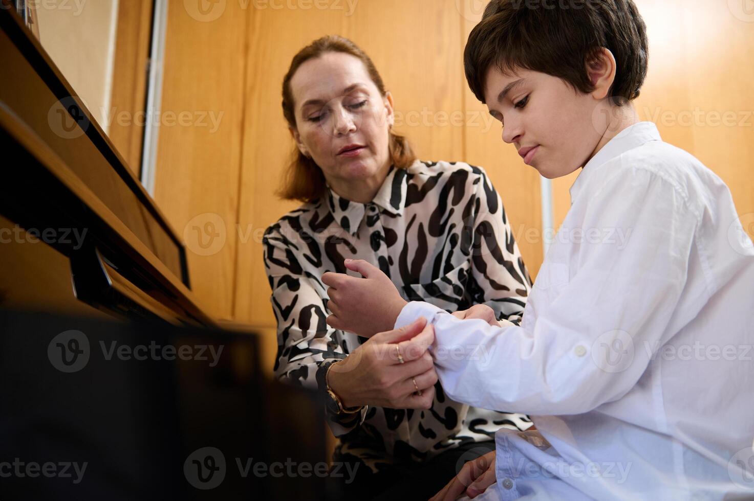 Pianist woman rolls up the sleeves on her student's shirt, prepares him for individual piano lesson photo