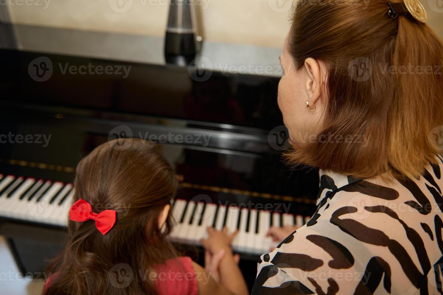 Learning to play the piano. Rear view of a female musician pianist giving a piano lesson to a little schoolgirl during individual music class photo