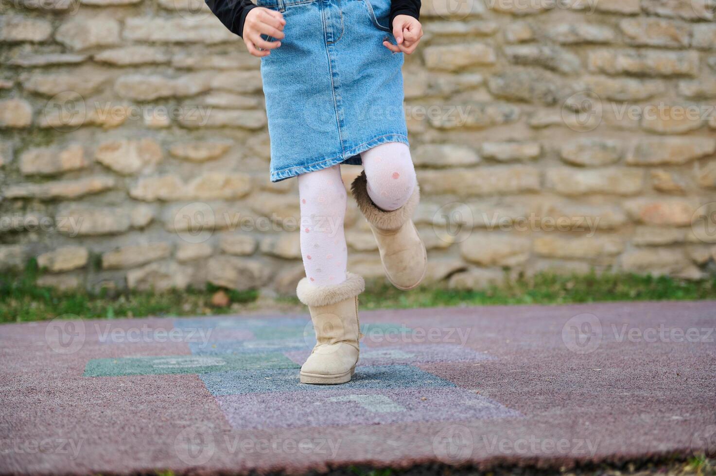 Details on legs of an active little child girl playing hopscotch, takes turns jumping over squares marked on the ground. photo