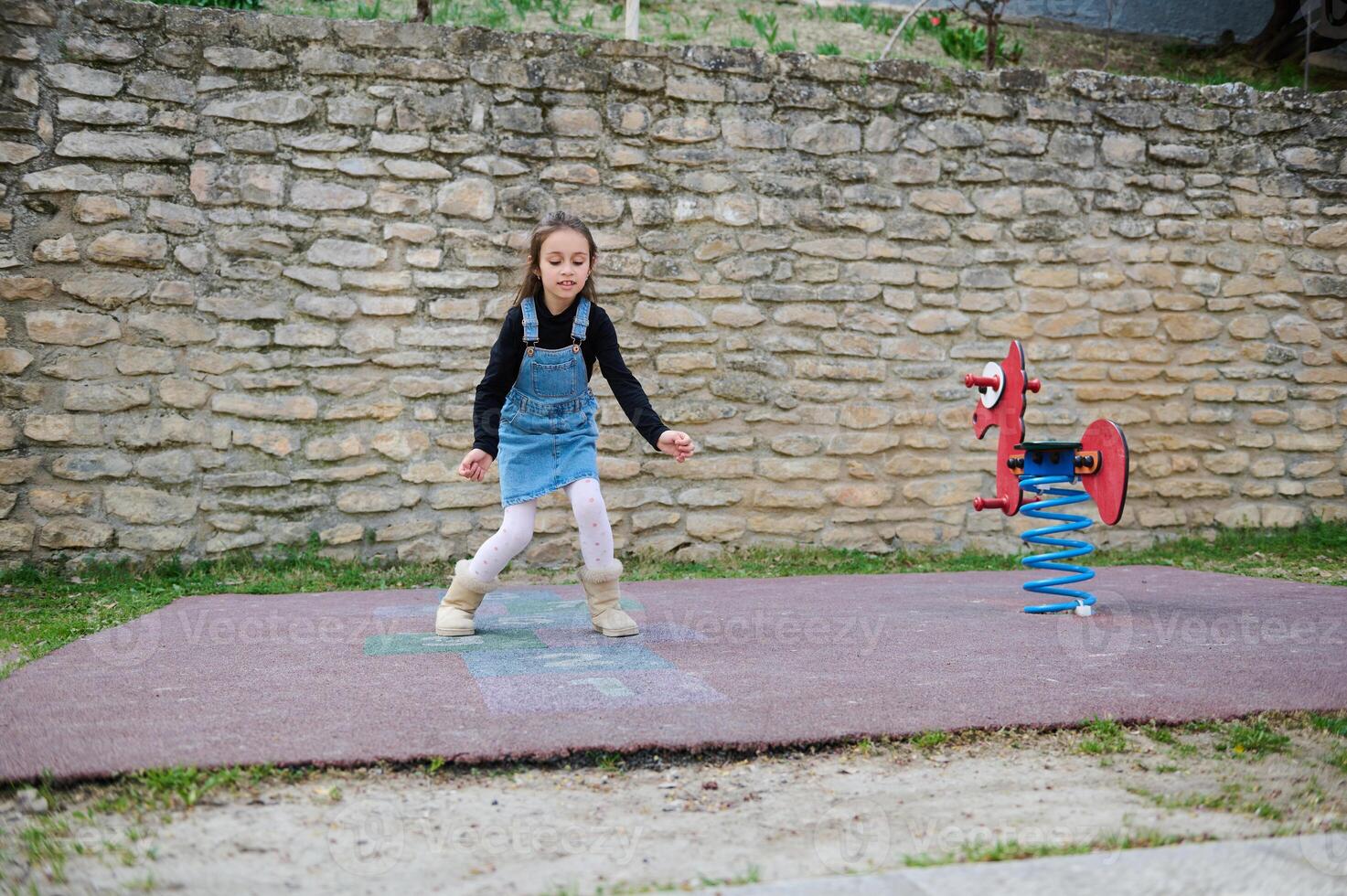 deportivo niño niña obras de teatro rayuela, toma vueltas saltando terminado cuadrícula marcado en suelo. niños y activo sano estilo de vida foto