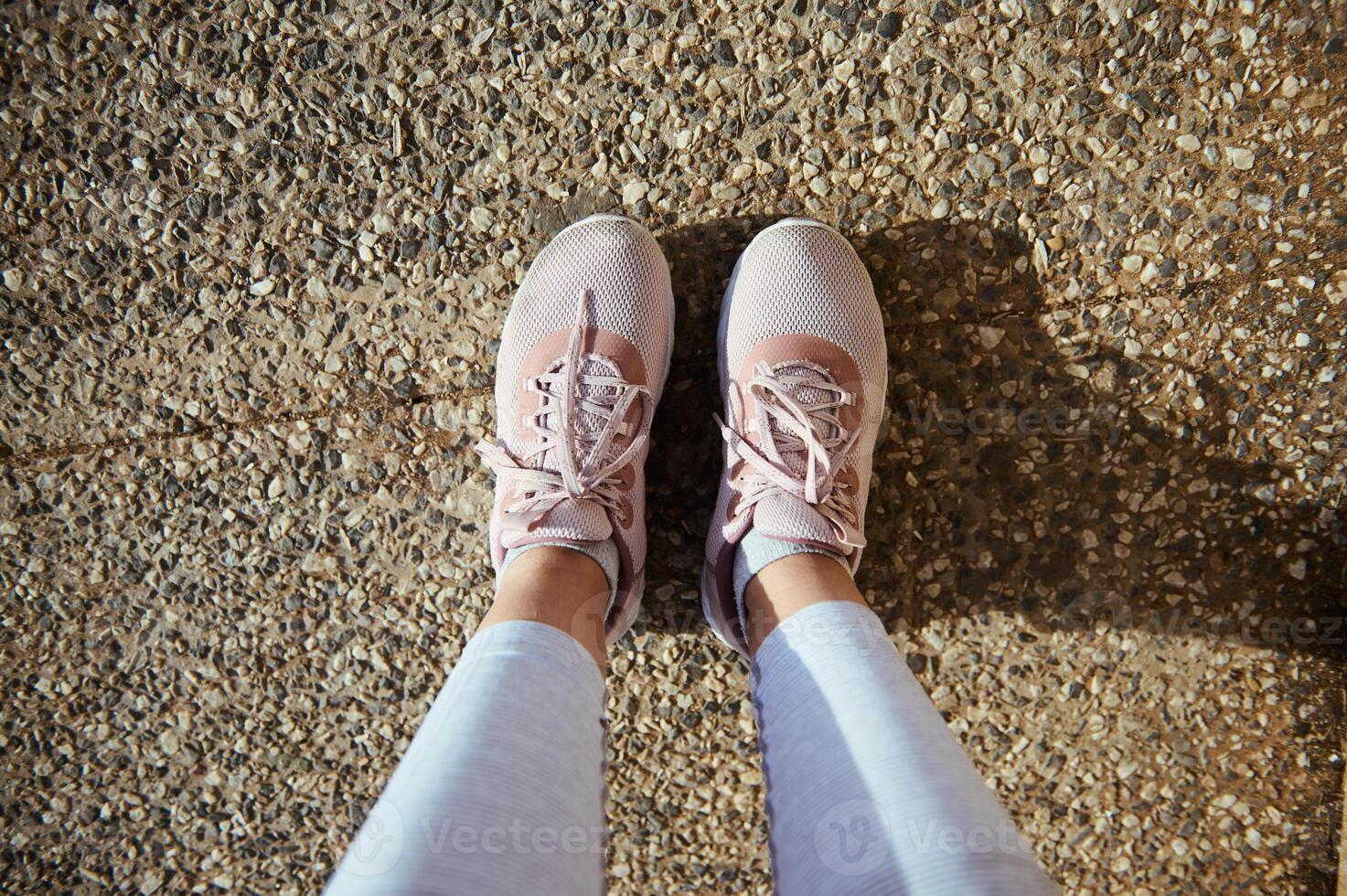 Sportswoman point of view. Legs and feet of female athlete in stylish running sports shoes, pink sneakers on the asphalt photo