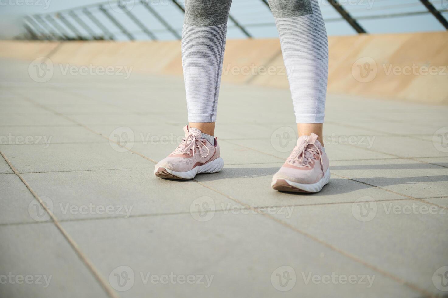 Female legs in pink sneakers running sports shoes and gray leggings on the treadmill on the city bridge. Copy ad space photo