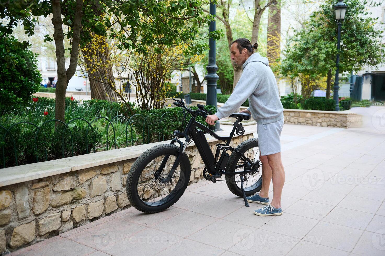 Full length of young man renting an electric bike for riding in the city. Electric bicycle - public eco transport photo