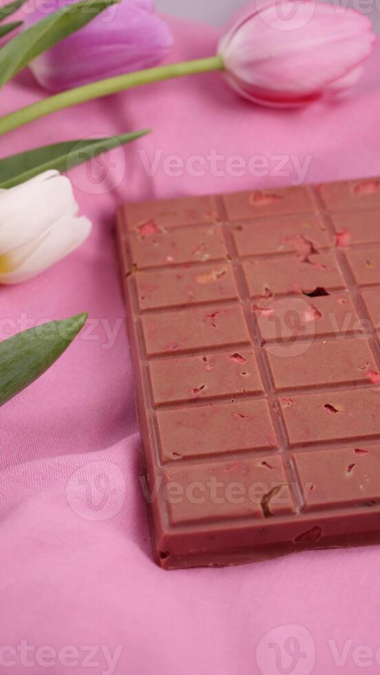 A bar of pink ruby chocolate with sublimated freeze-dried strawberries and almonds and spring tulip flowers . A dessert based on berries and nuts for International Women's Day, March 8, mother's day photo