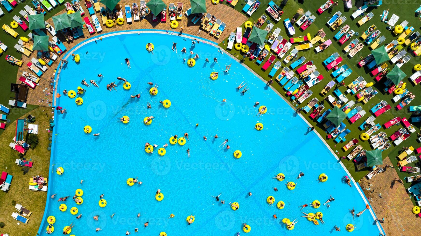 Top view of people relaxing in the pool on yellow inflatable circles and sun beds on the beach photo