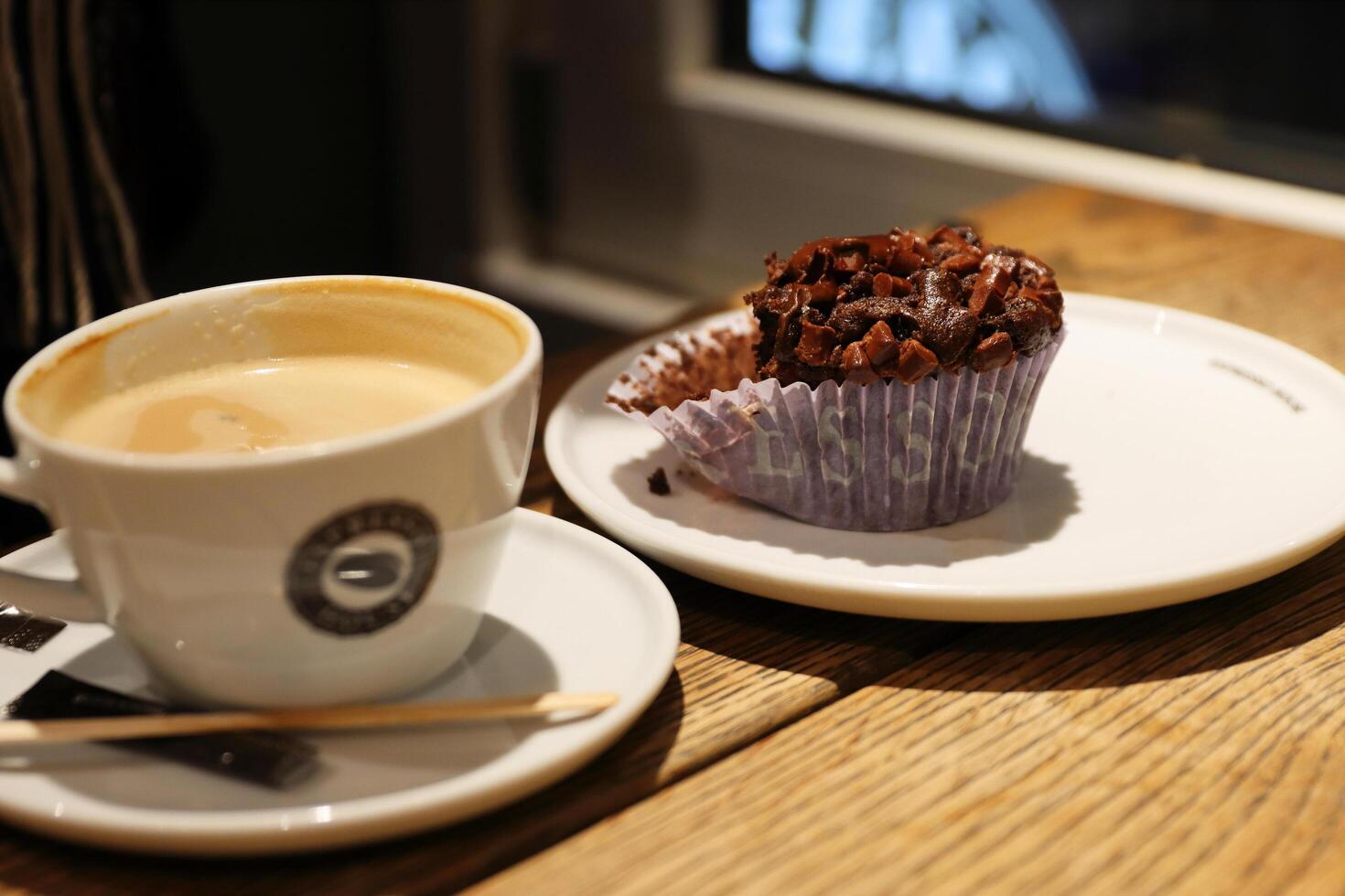Copenhagen, Denmark - February, 20th, 2023. Espresso House. A cup of cappuccino with milk foam and delicious homemade chocolate cupcake on the vintage wooden table. Selective focus photo