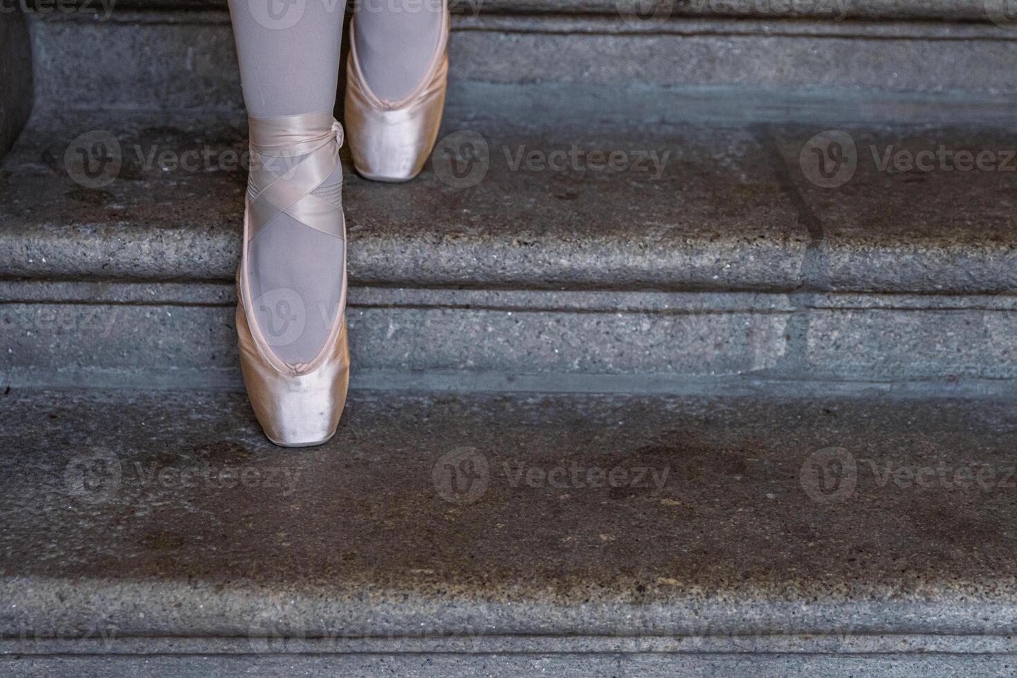 Closeup of ballerina's pointes on the gray stone steps background. Dance sitting on the steps. Ballerina feet with pink ballet slippers on. Minimalistic, simple. Copy space. photo