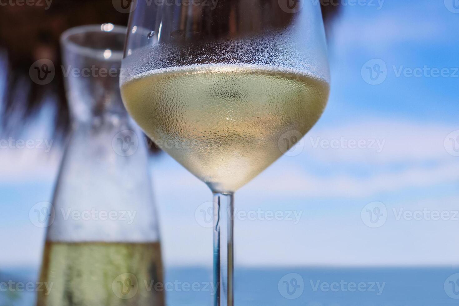 Glass and the pitcher of ice cold vine on the table in the restaurant on the Adriatic beach in Durres, Albania. Beautiful sunny summer day. Blue sky and the sea. Selective focus photo