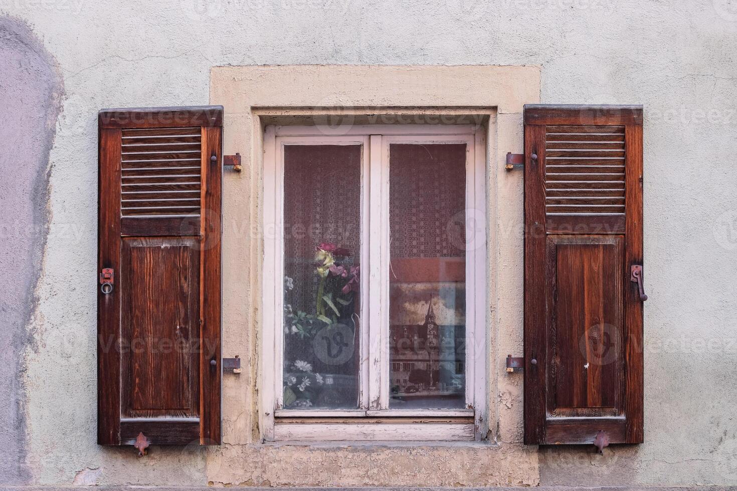 Country style window with old dried flowers, retro wooden shutters, an old photograph behind the glass and white net curtains tulle. Antique German historical house in Bavaria. Shabby textured wall. photo