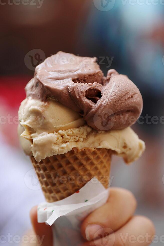 Closeup of the girl's hand holding waffle cone with 2 scoops of traditional Italian ice-cream called Gelato. Ice-cream cone wrapped with napkin. Blurred background. Selective focus. photo