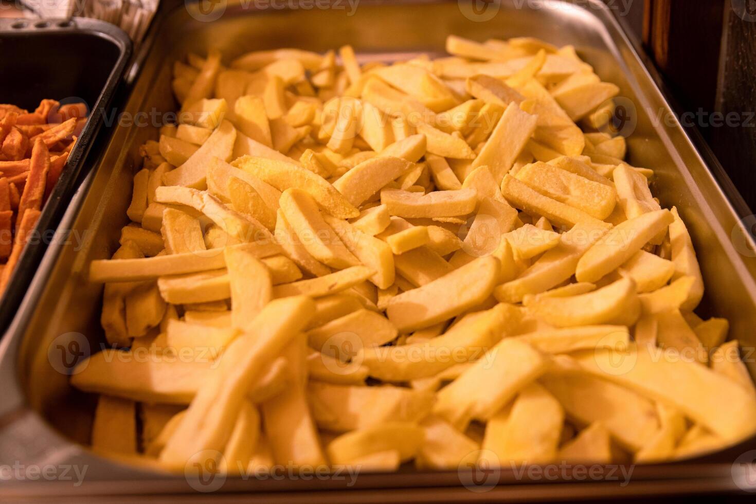 Yummy French fries in the metal tray. Potato chips on the counter at the street market. Selective focus. Side view. Bokeh. photo