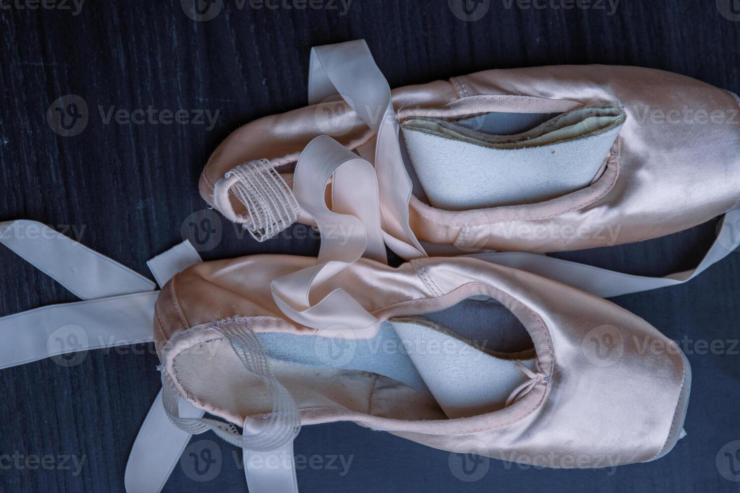 Close-up of Pair of used Ballet pointe shoes. Ballet dance slippers with a bow of ribbons on a dark background. Gray dark background. Top view. photo