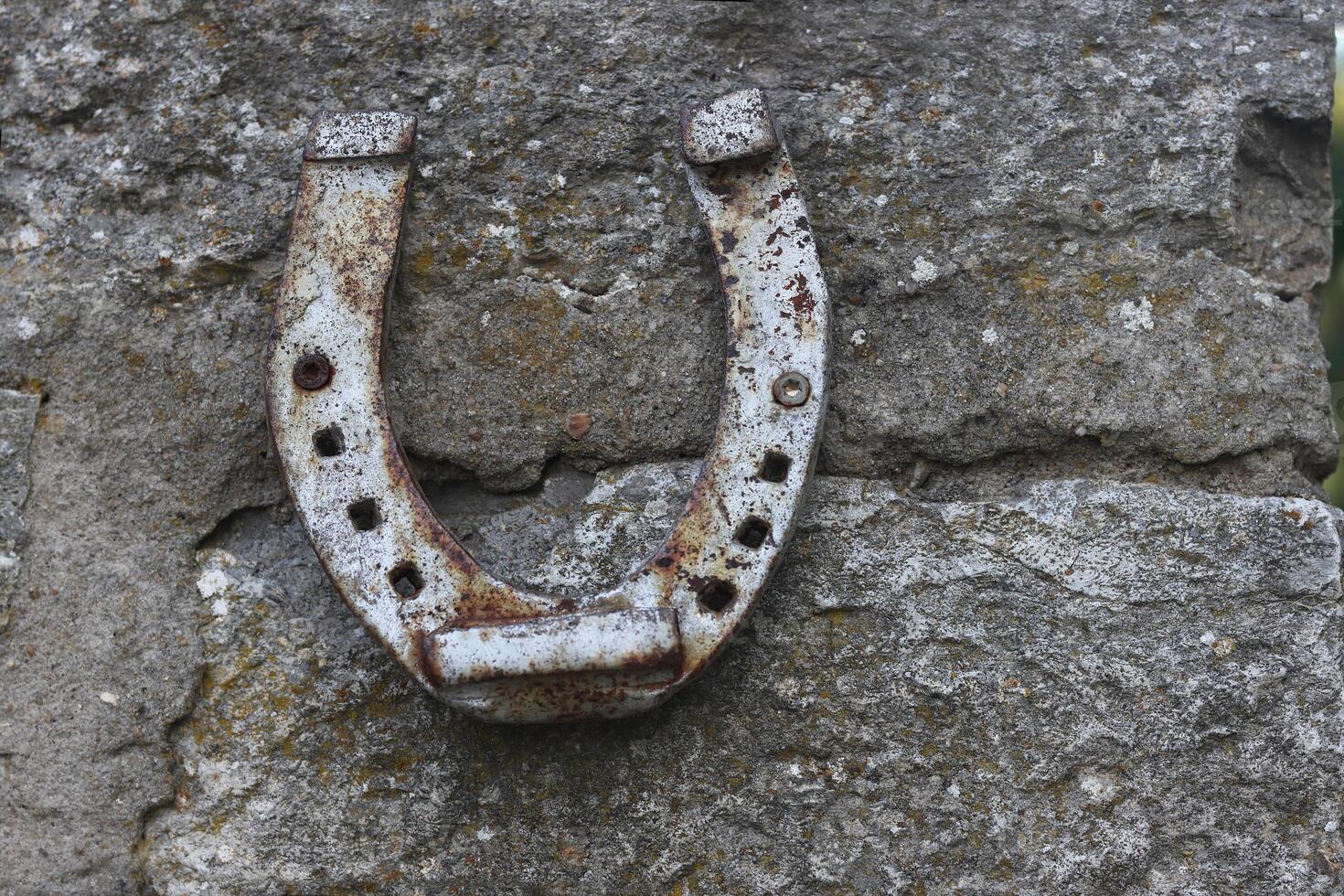 Close up of an old gray rusted horseshoe hanging on the stone wall. Antique rust horse shoe on the concrete texture with cracks and cement patches. Symbol of good luck and wealth. Selective focus photo