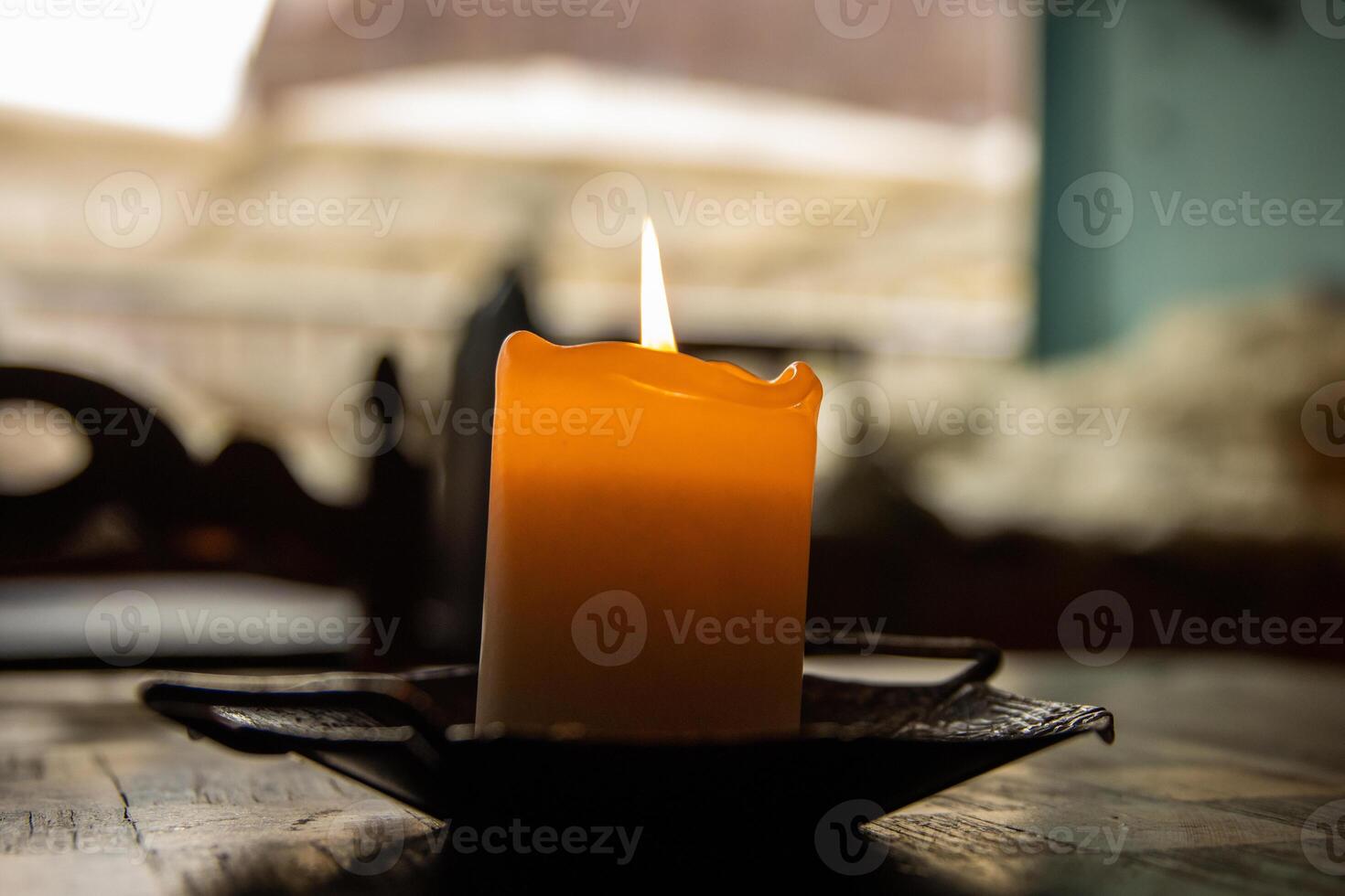 hermosa ardiente naranja hecho a mano natural cera vela en café de madera mesa. ventana en el borroso antecedentes. antiguo metal hierro vela poseedor. acogedor romántico atmósfera. cerca arriba. selectivo atención foto