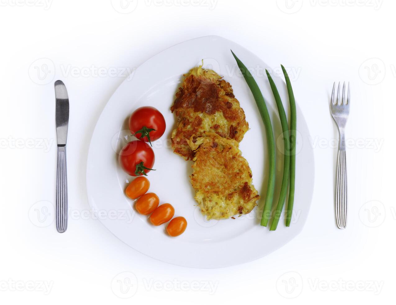 Homemade fried grated potato pancakes served with fresh tomatoes and green onions on the white plate, fork and knife. Draniki. Top view. Cutout and isolated with clipping path on the white background photo