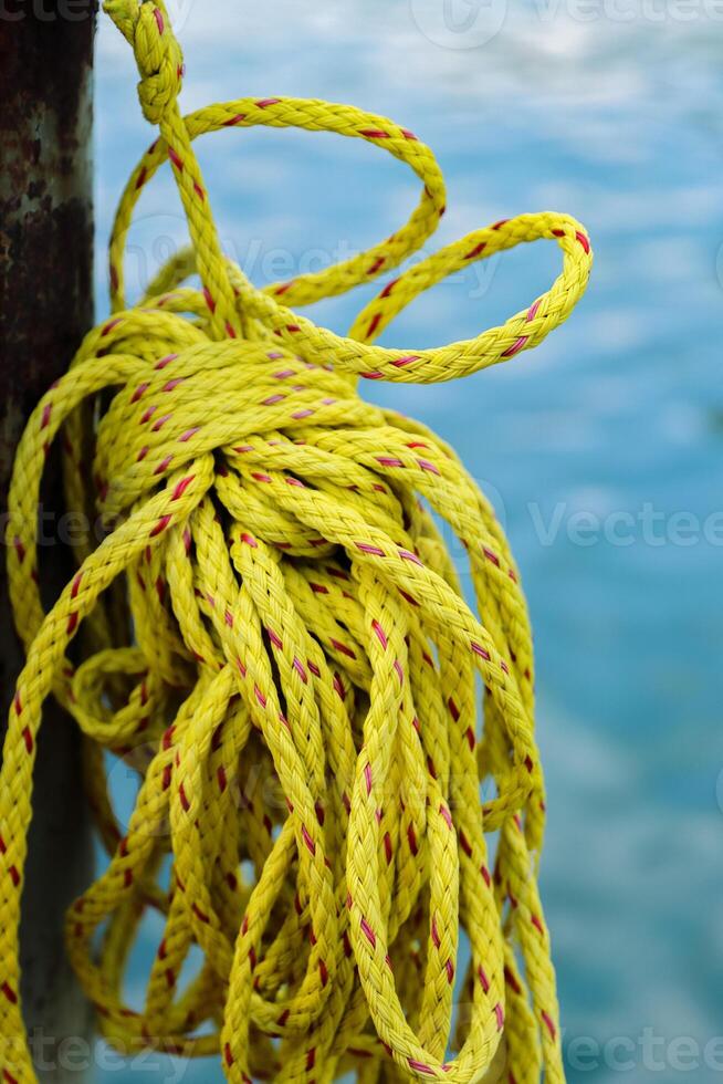 Yellow sailing Rope Coil hanging on the wooden bollard in harbor. Blue sea water on the blurred background. Closeup. Selective focus photo