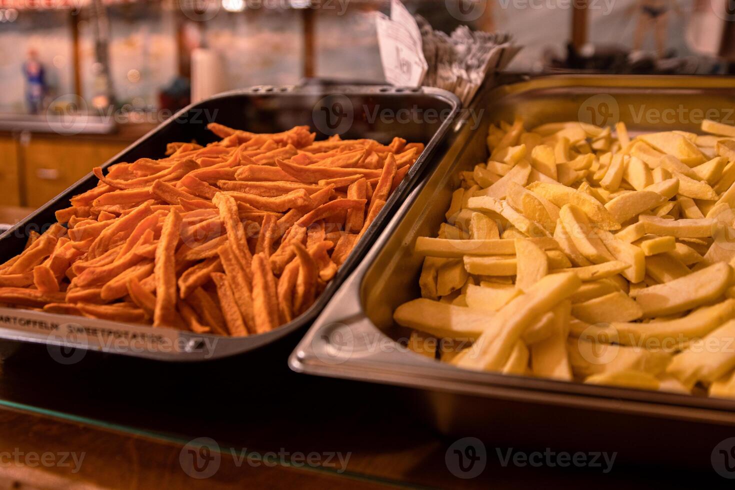 To kinds of Yummy French fries in the metal trays. Potato chips on the counter at the street market. Selective focus. Side view. Bokeh. photo