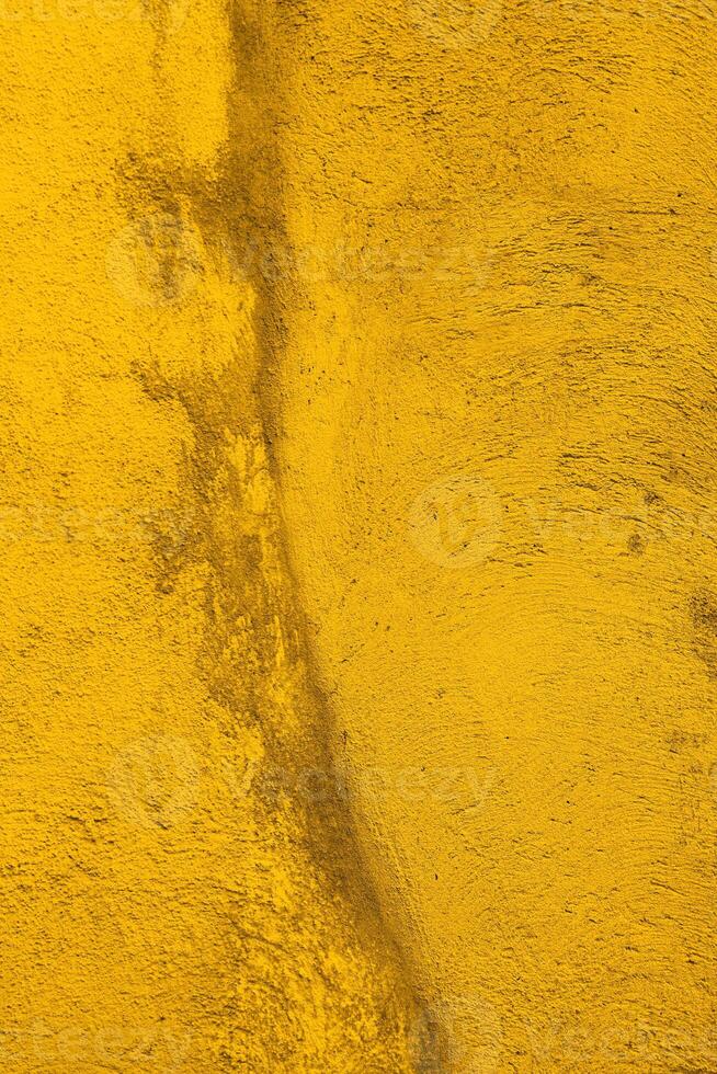 Texture of  old concrete wall painted into deep Vibrant warm golden yellow color. Decorative plaster. Abstract design grunge background. Crack on the wall surface. Vintage, retro, ancient house photo