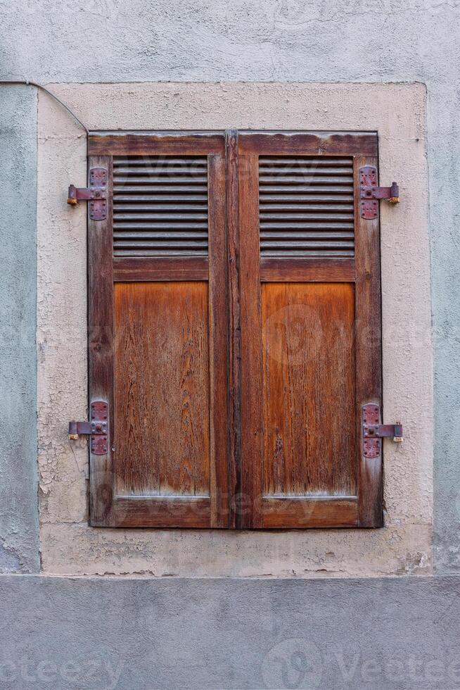 Country style window with closed ancient retro wooden shutters. Antique German historical house in Bavaria. Shabby cracked textured wall. Historic and atmospheric architect element. Front view photo