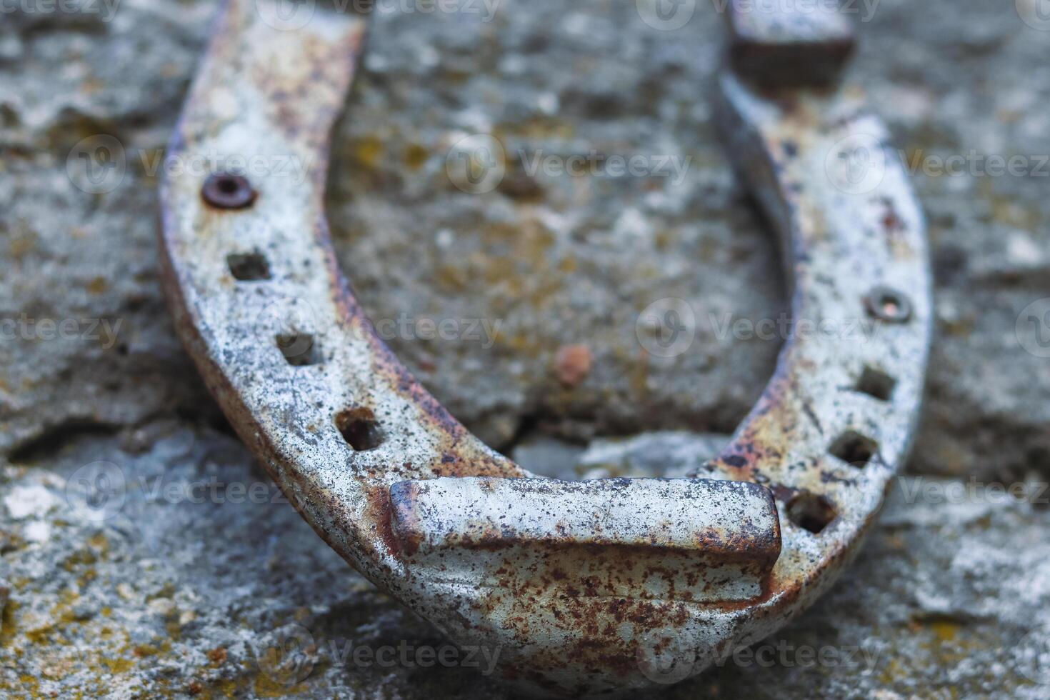 Close up of an old gray rusted horseshoe hanging on the stone wall. Antique rust horse shoe on the concrete texture with cracks and cement patches. Symbol of good luck and wealth. Selective focus photo