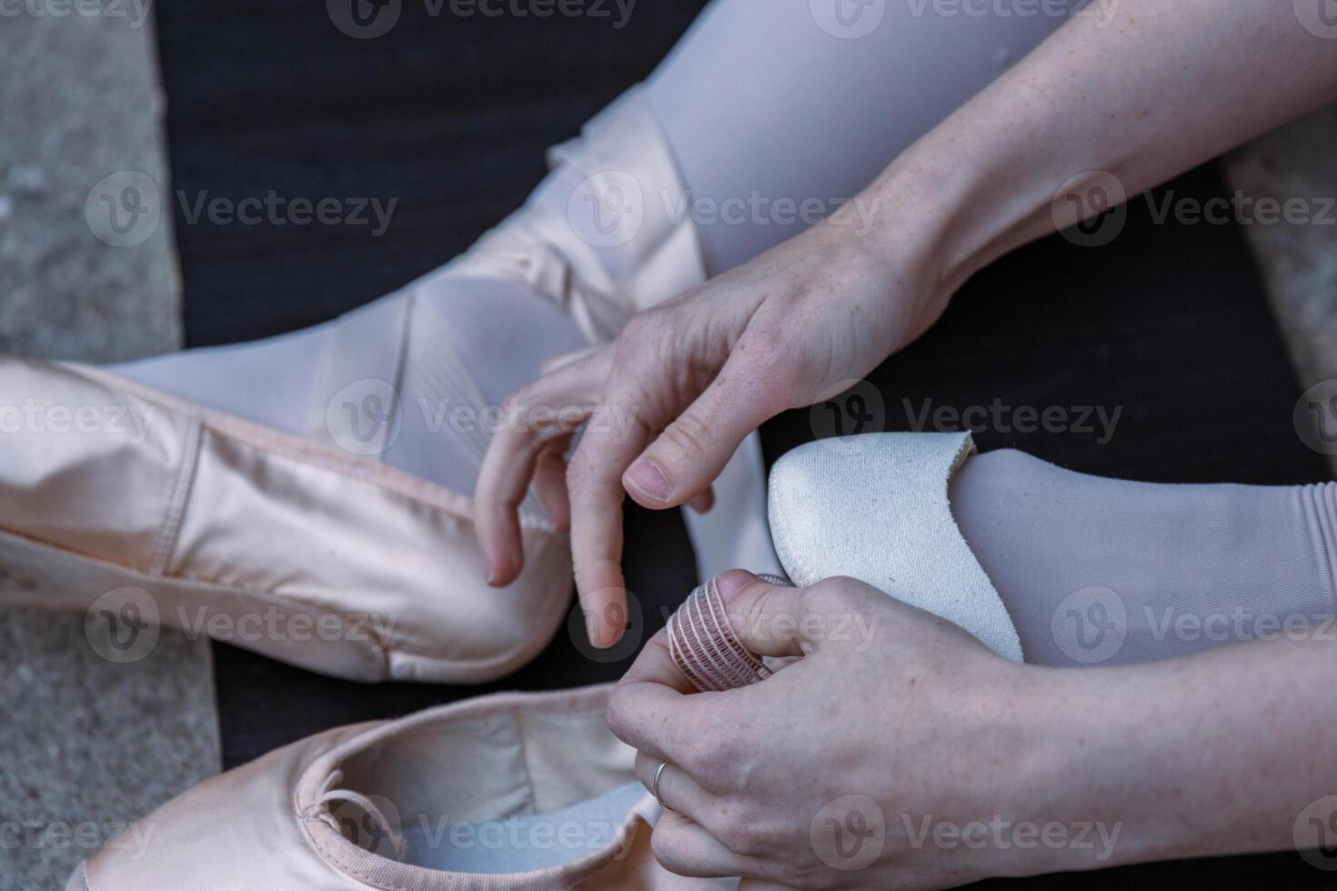 Ballerina is putting on her pointe shoes sitting on the stone floor. Ballet dancer tying ballet shoes. Dance student is preparing to the performance. Close-up photo