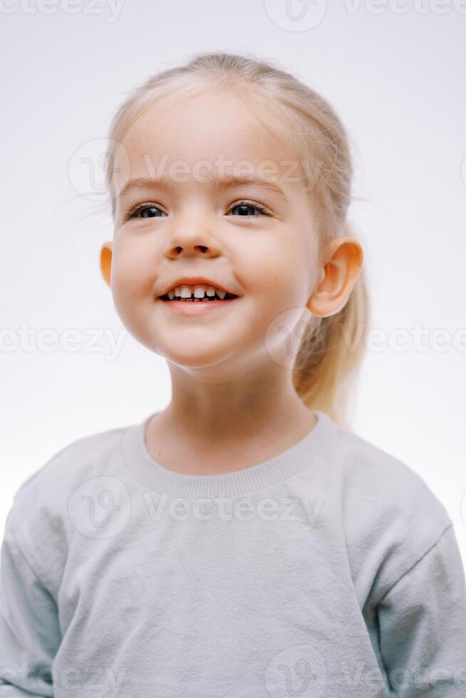 retrato de un pequeño sonriente niña en alegre anticipación en un gris antecedentes foto