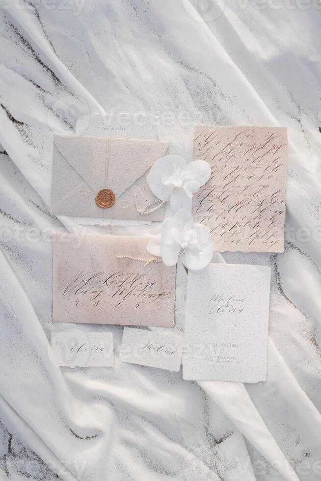 Wedding invitations with name cards lie next to envelopes and flowers on a white cloth photo