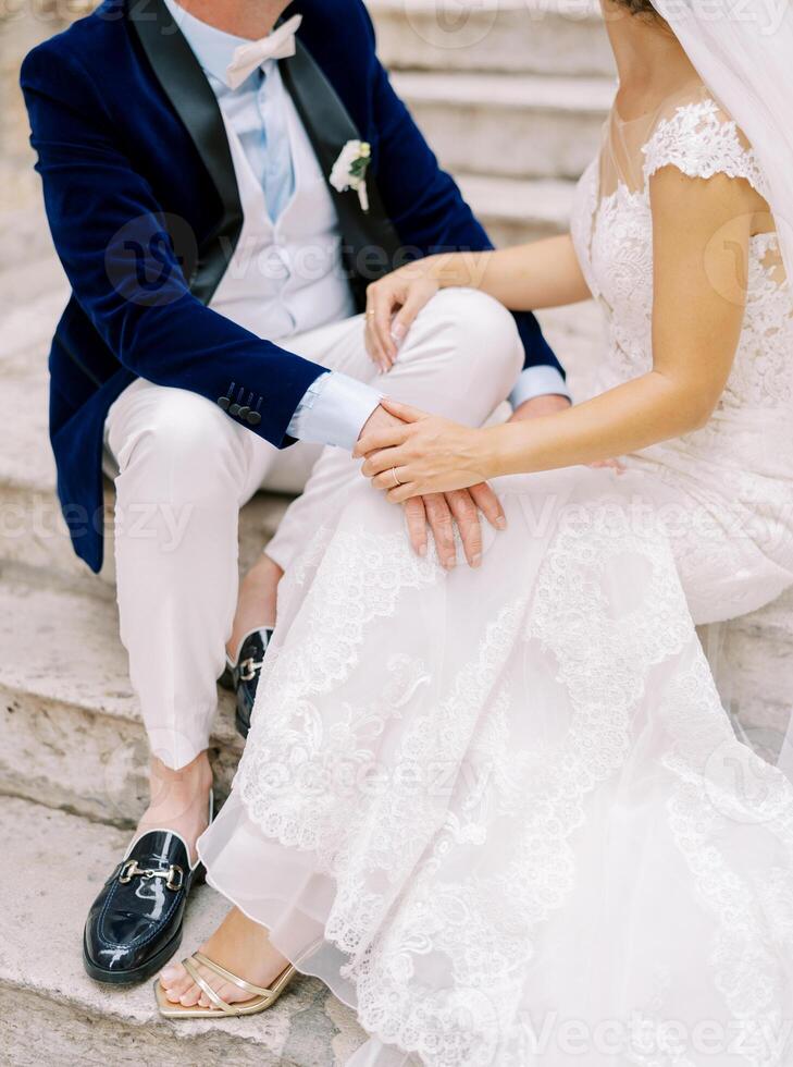 novia y novio sentar en antiguo Roca pasos y sitio su manos en cada otro vueltas. recortado sin rostro foto