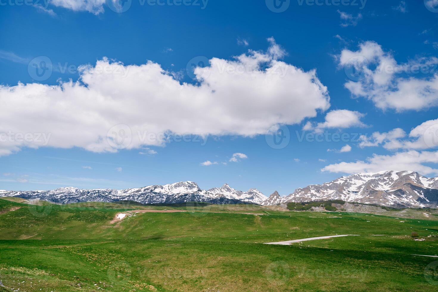 Hilly green lawn at the foot of the snowy mountains photo