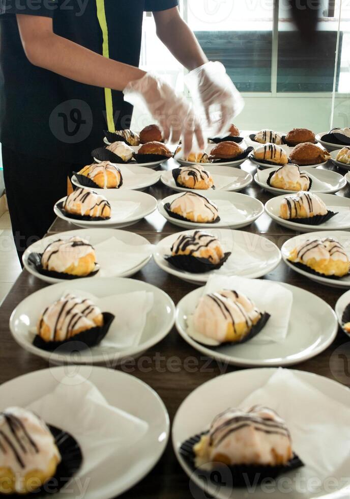 hotel employees are preparing snack cakes on plates before the meeting. Many rows of plates with buffet snacks. photo