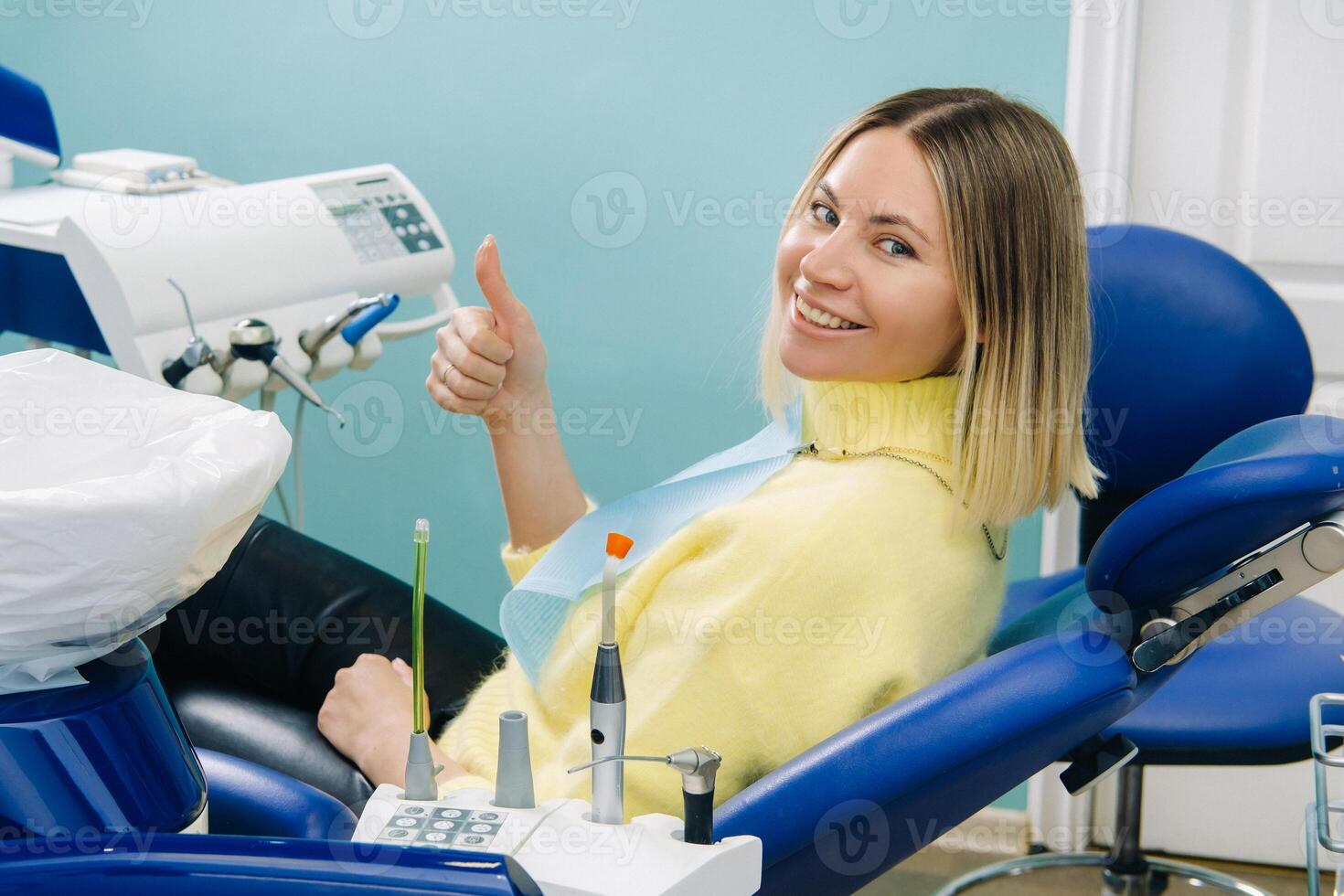 Beautiful girl patient shows the class with her hand while sitting in the Dentist's chair photo