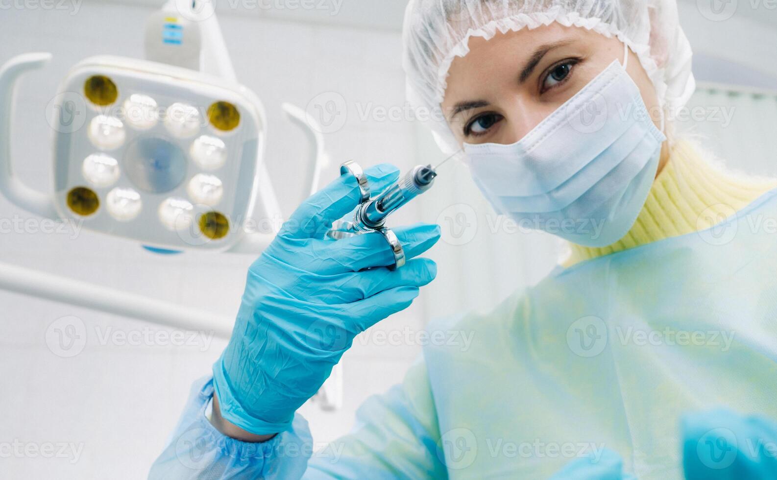 A masked dentist holds an injection syringe for a patient in the office photo