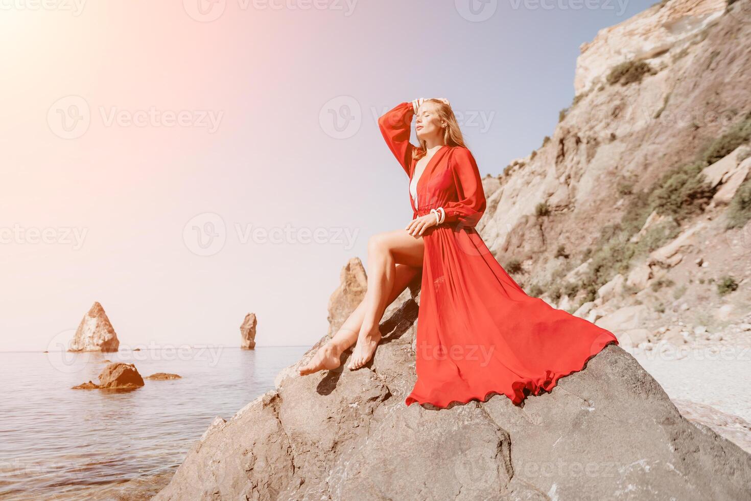 Woman travel sea. Young Happy woman in a long red dress posing on a beach near the sea on background of volcanic rocks, like in Iceland, sharing travel adventure journey photo