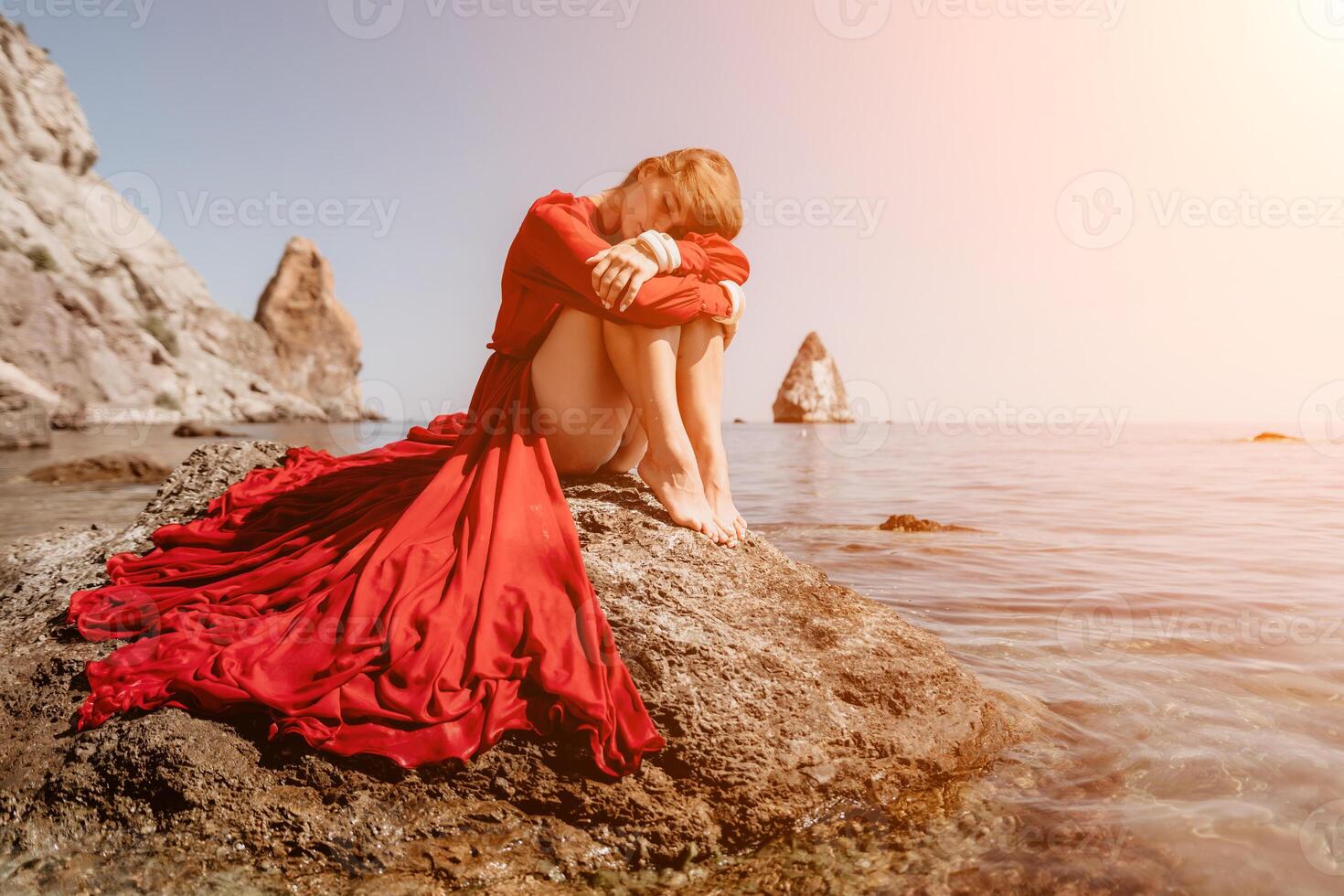 Woman travel sea. Happy tourist in red dress enjoy taking picture outdoors for memories. Woman traveler posing on the rock at sea bay surrounded by volcanic mountains, sharing travel adventure journey photo