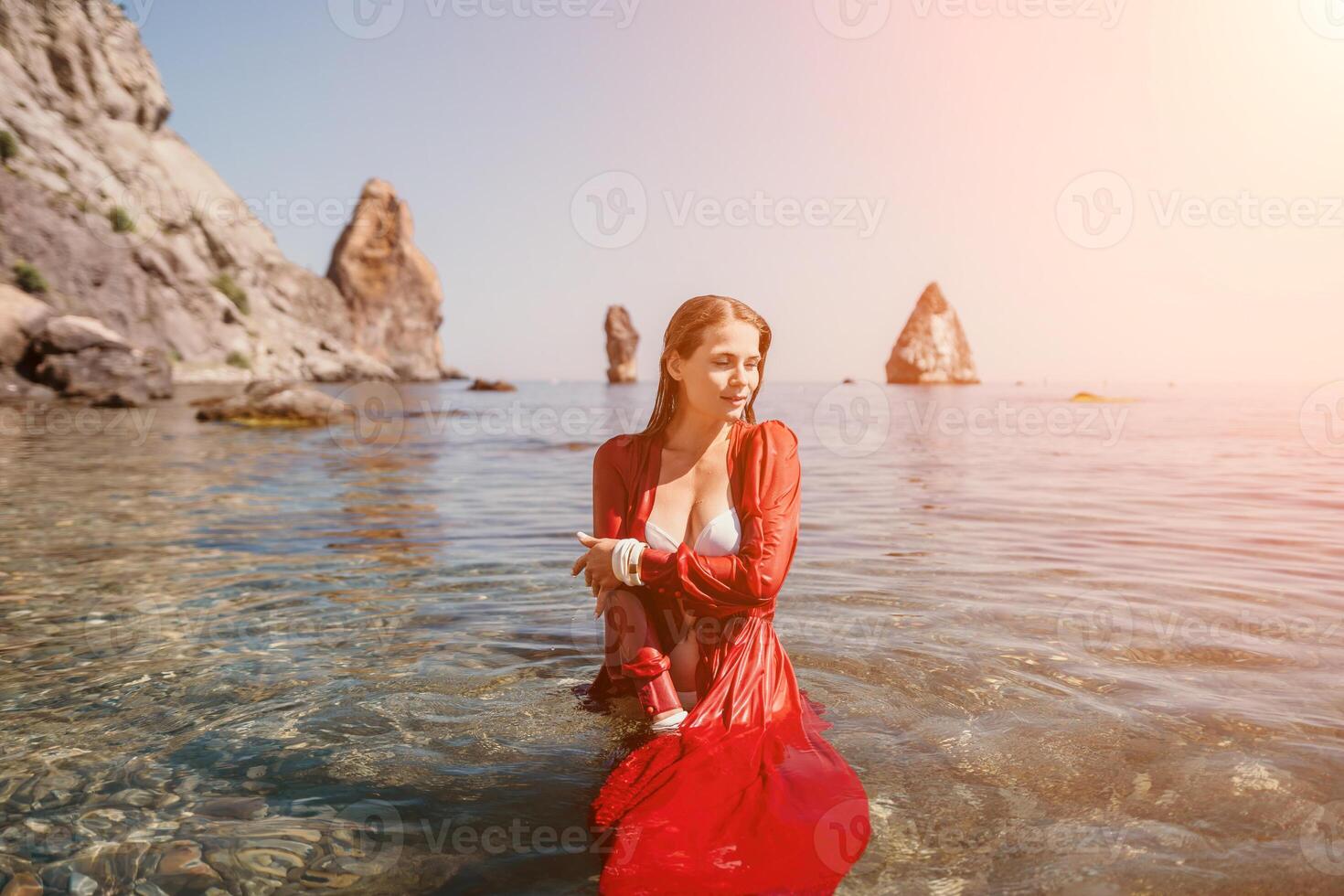 Woman travel sea. Happy tourist in red dress enjoy taking picture outdoors for memories. Woman traveler posing in sea beach, surrounded by volcanic mountains, sharing travel adventure journey photo