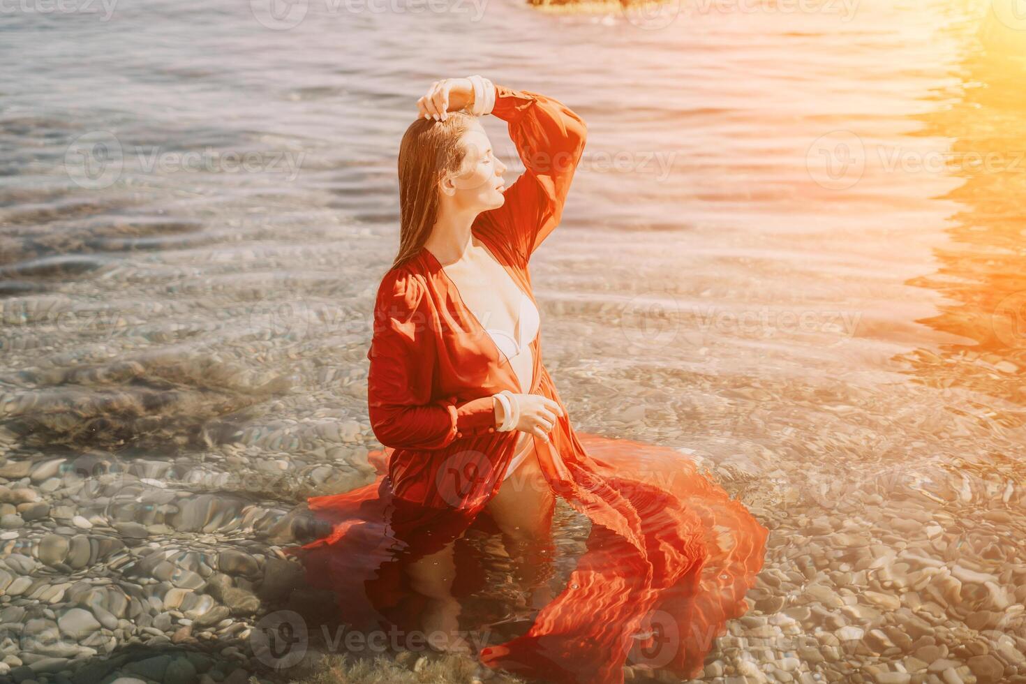 mujer viaje mar. contento turista en rojo vestir disfrutar tomando imagen al aire libre para recuerdos. mujer viajero posando en mar playa, rodeado por volcánico montañas, compartiendo viaje aventuras viaje foto