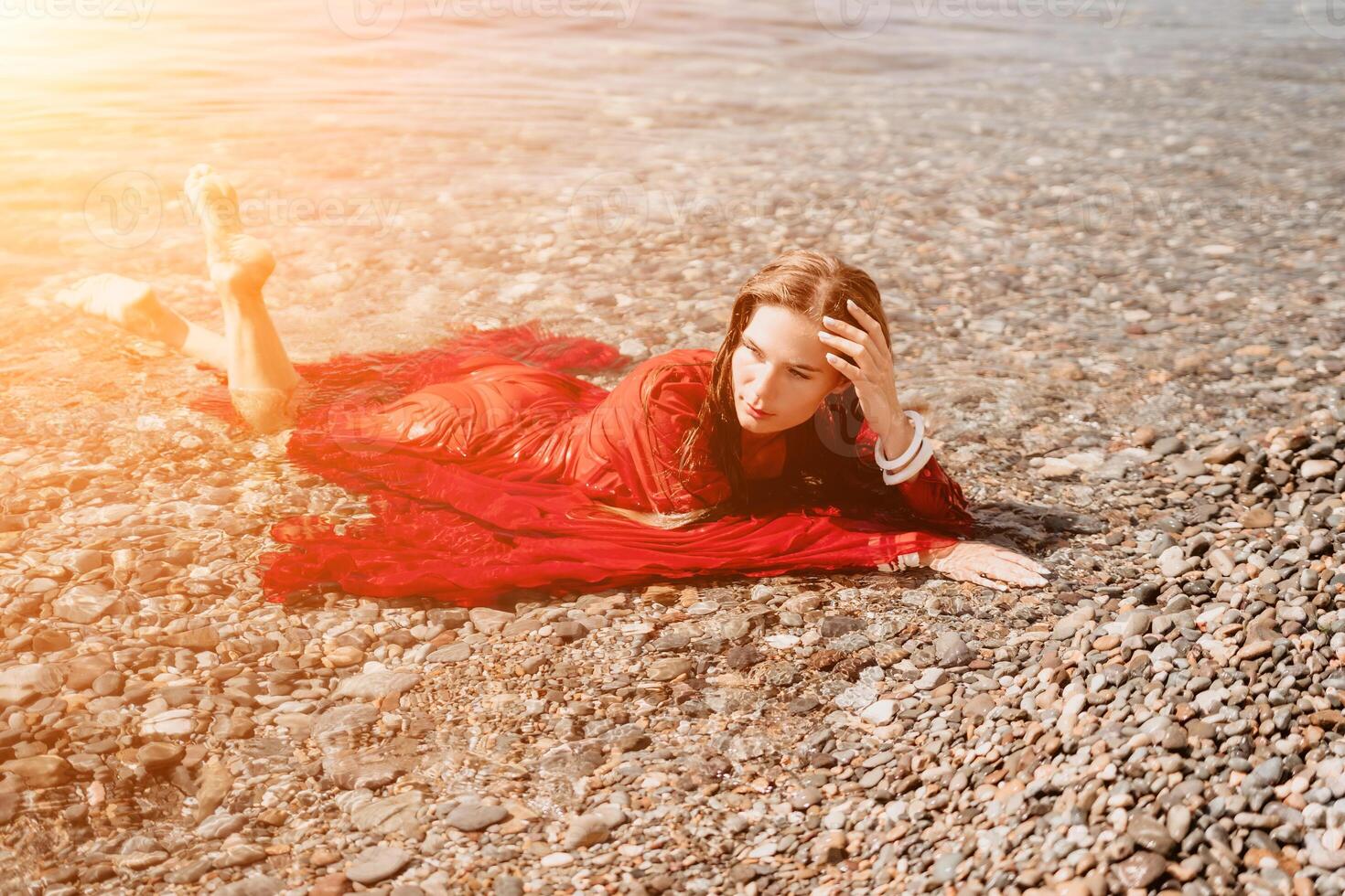 Woman travel sea. Happy tourist in red dress enjoy taking picture outdoors for memories. Woman traveler posing in sea beach, surrounded by volcanic mountains, sharing travel adventure journey photo