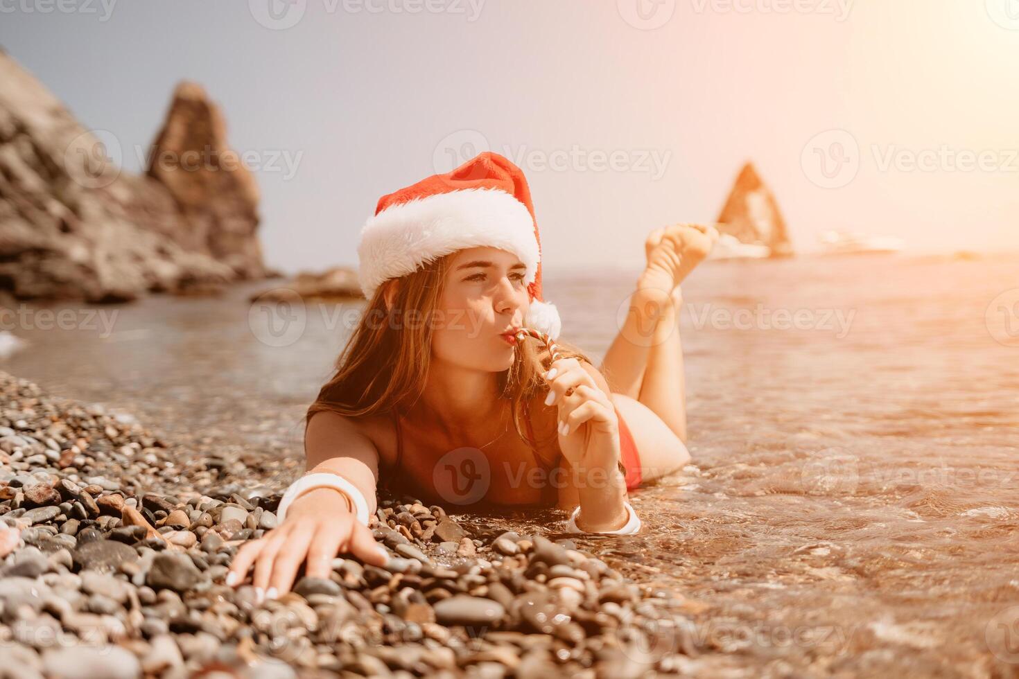 Woman travel sea. Happy tourist enjoy taking picture on the beach for memories. Woman traveler in Santa hat looks at camera on the sea bay, sharing travel adventure journey photo
