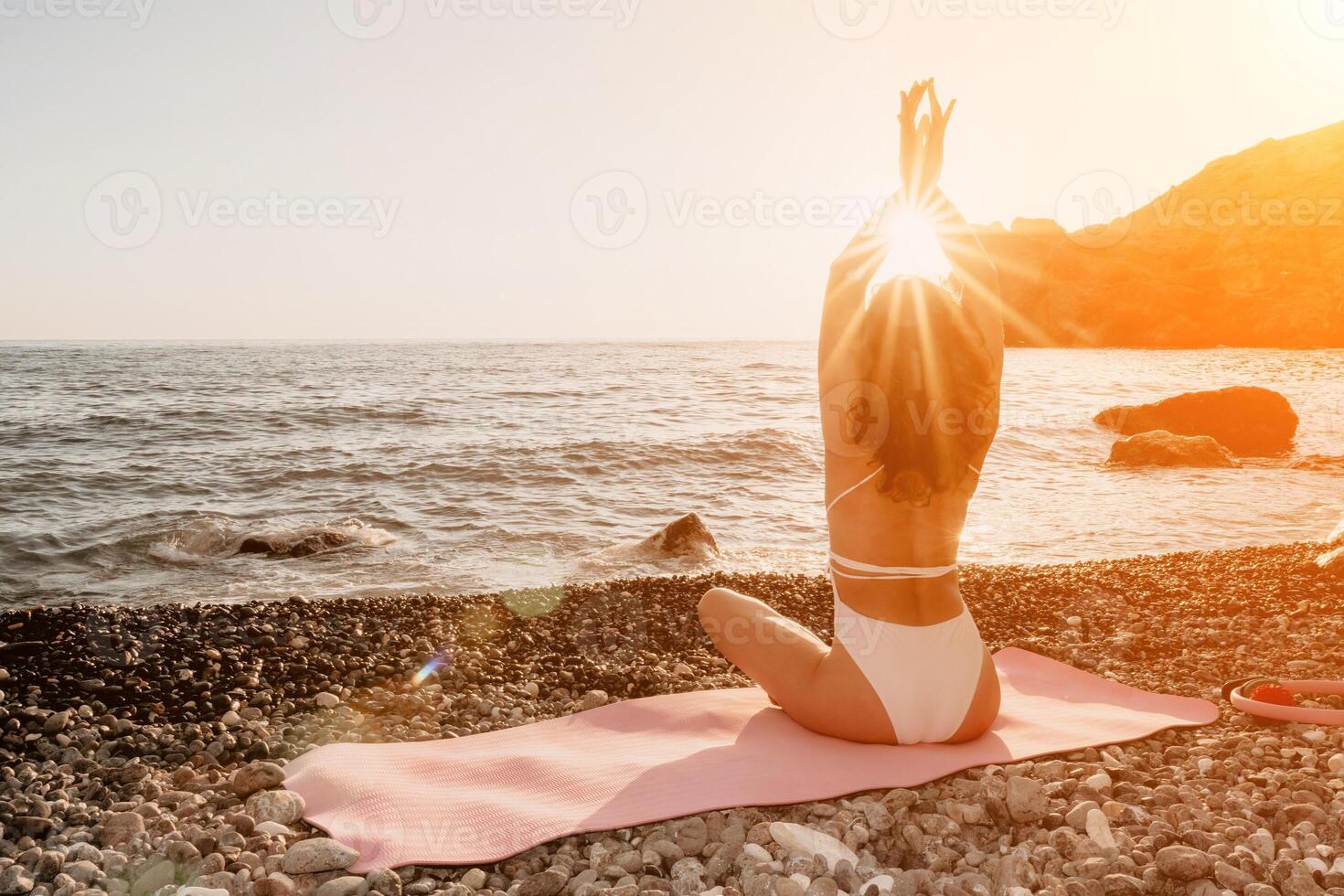 Woman sea yoga. Happy woman in white swimsuit and boho style braclets practicing outdoors on yoga mat by sea on sunset. Women yoga fitness routine. Healthy lifestyle, harmony and meditation photo