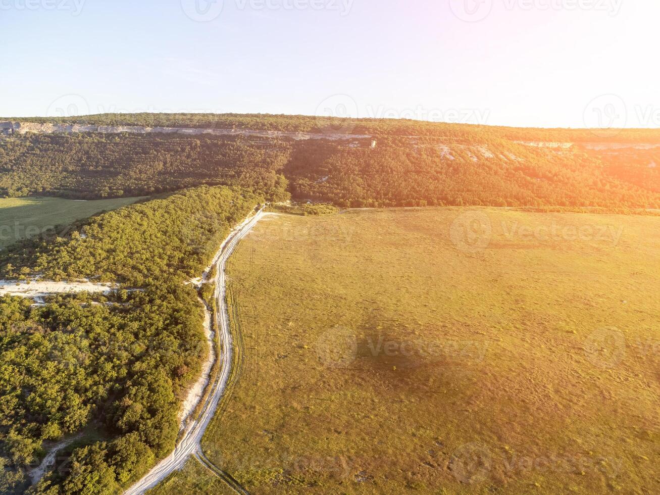 Aerial view on green wheat field, road and hills in countryside. Field of wheat blowing in the wind on sunset. Ears of barley crop in nature. Agronomy, industry and food production. photo