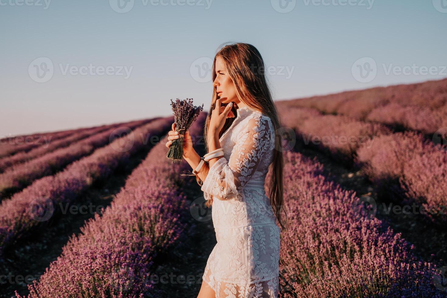 Woman lavender field. Happy carefree woman in a white dress walking in a lavender field and smelling a lavender bouquet on sunset. Ideal for warm and inspirational concepts in wanderlust and travel. photo