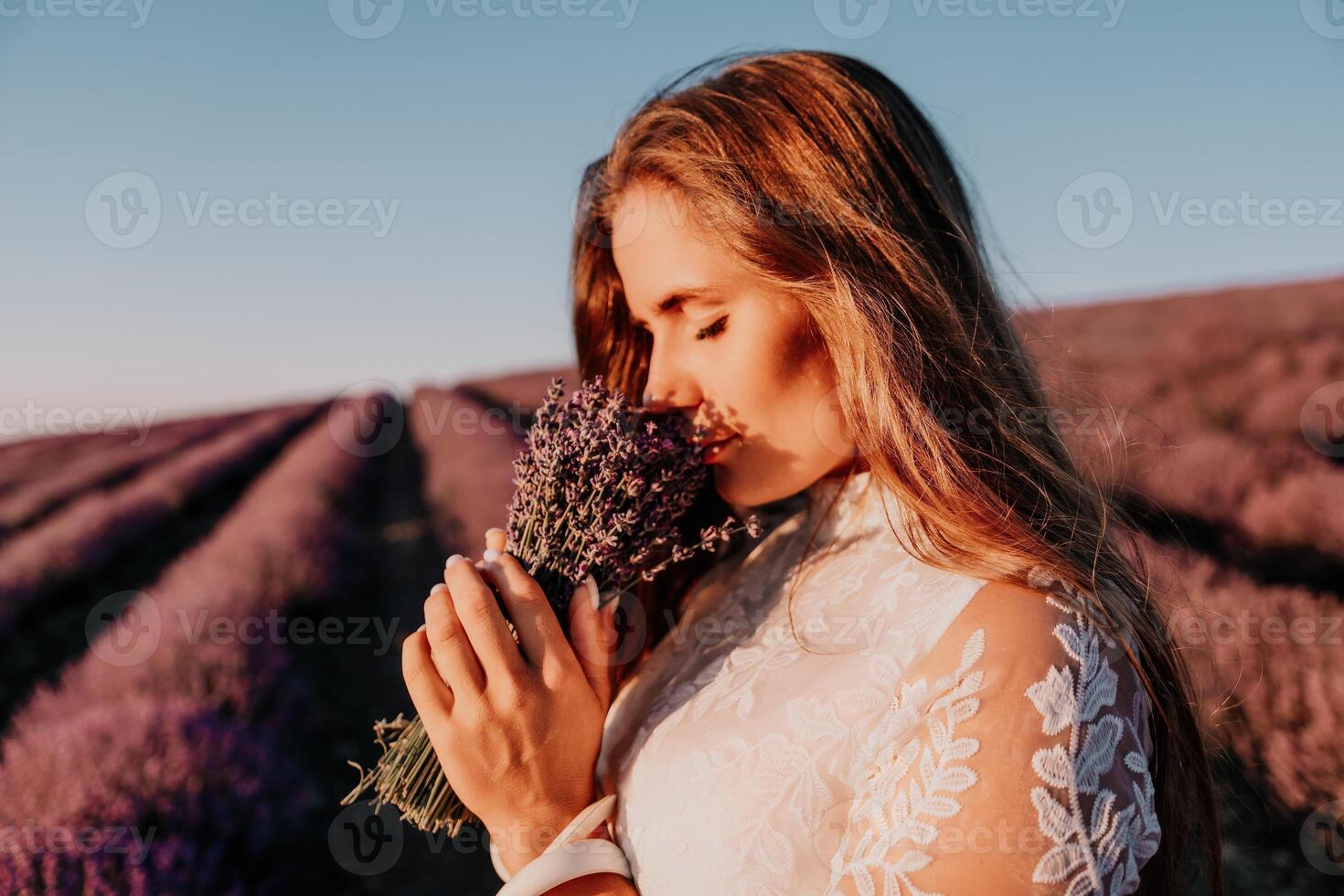 Woman lavender field. Happy carefree woman in a white dress walking in a lavender field and smelling a lavender bouquet on sunset. Ideal for warm and inspirational concepts in wanderlust and travel. photo