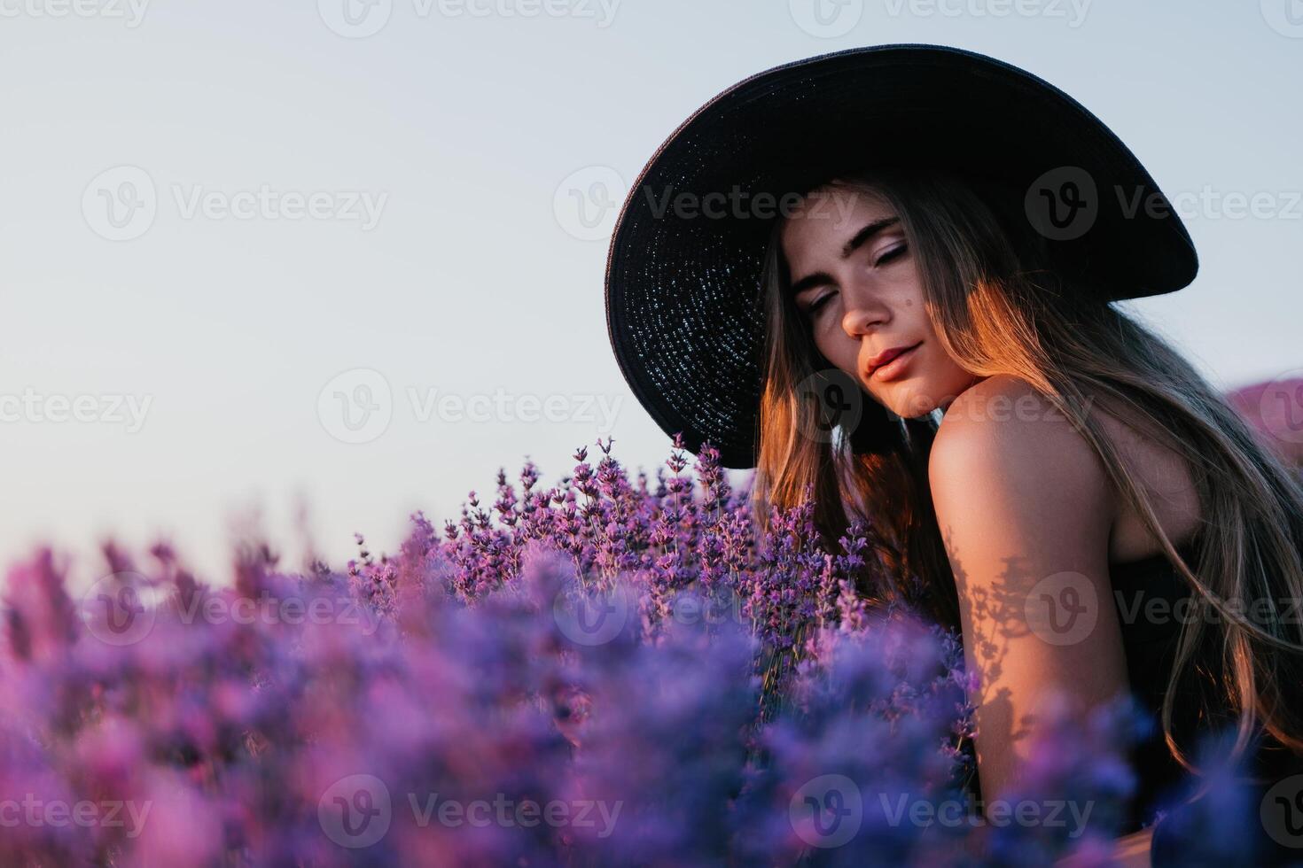 Woman lavender field. Happy carefree woman in black dress and hat with large brim smelling a blooming lavender on sunset. Perfect for inspirational and warm concepts in travel and wanderlust. Close up photo